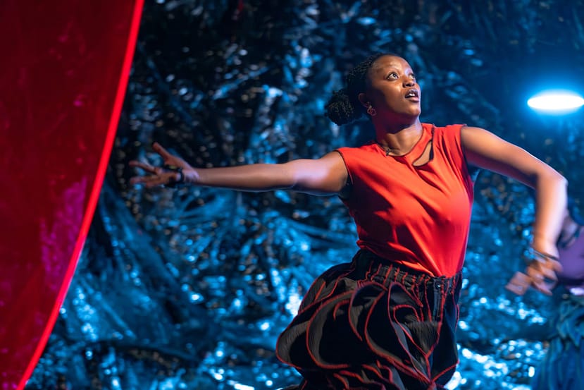single black female dancer extends right arm out her side and left in front of her, looking up, against blue background